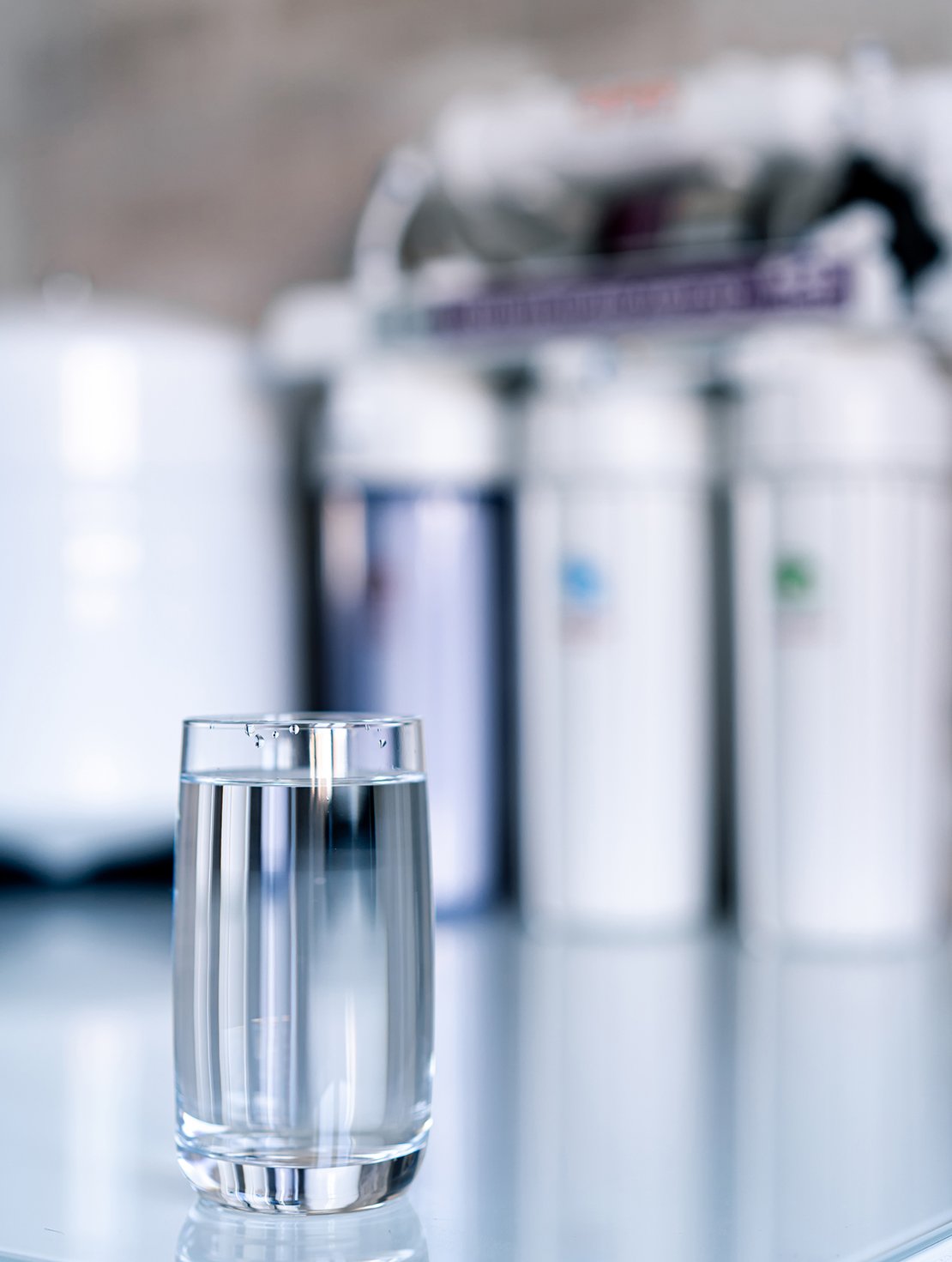 Household filtration system. Water treatment concept. Use of water filters at home. Glass of clean water and filters on a blurred background.